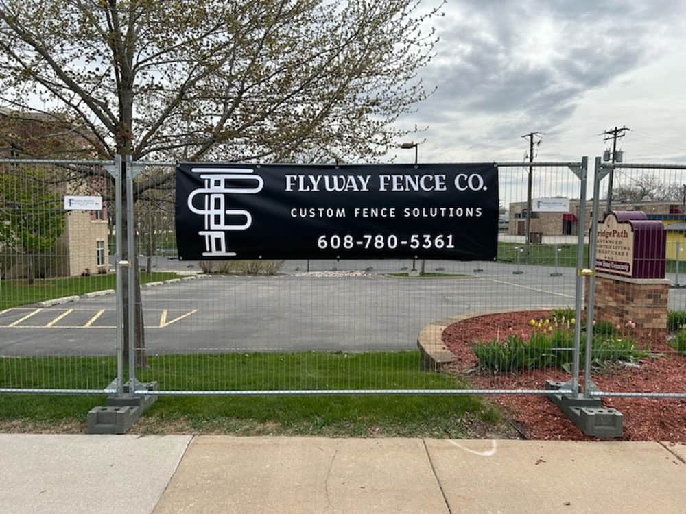 A black banner on a metal fence reads 